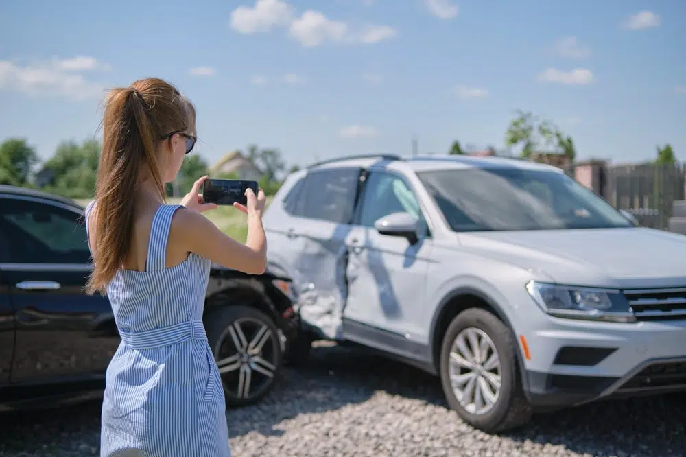 Stressed driver taking picture on cellphone camera of smashed vehicle calling for emergency service help after car accident.
